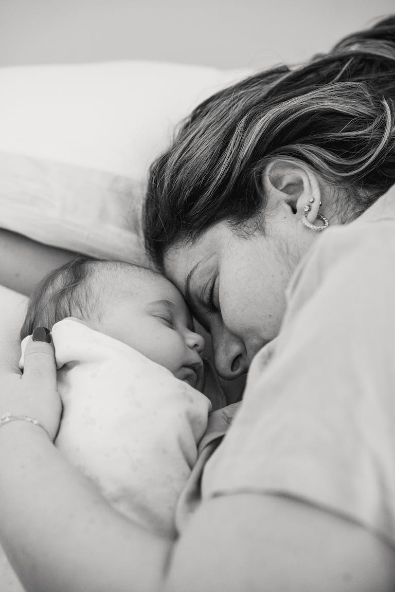 Peaceful young mother with baby embracing and sleeping on bed